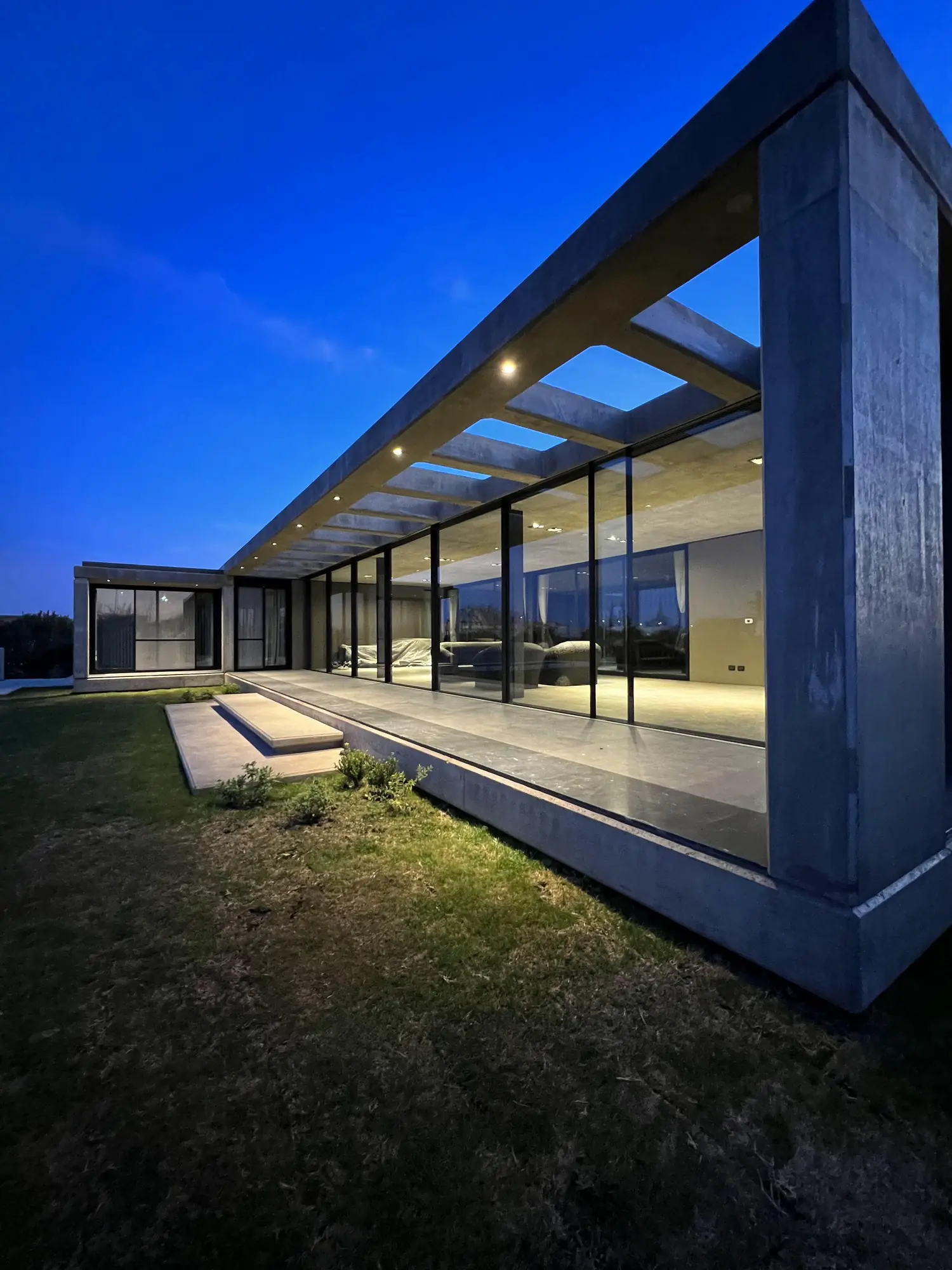 Galería de hormigón y vidrio al anochecer, en una vivienda de Invernón Arquitectos en Córdoba