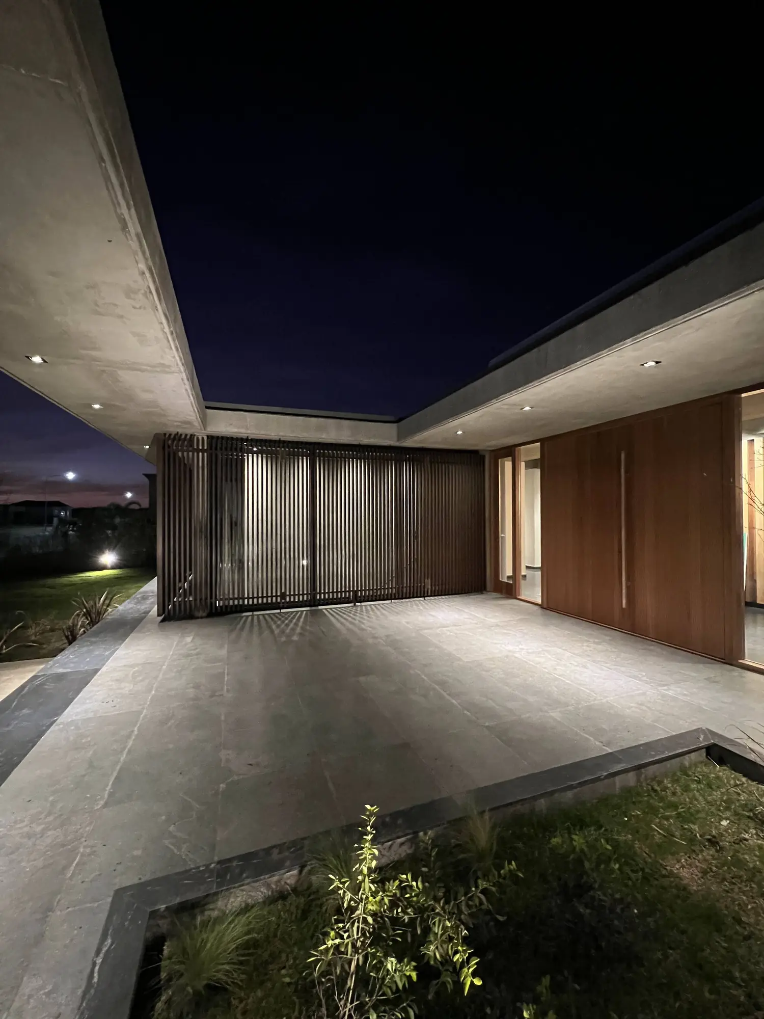 Entrada con puerta de madera y celosía de listones, iluminada de noche